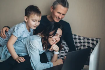 Kanepede anne, baba ve küçük oğlun gülümseyerek birlikte dizüstü bilgisayar ekranına baktığı ev ortamı