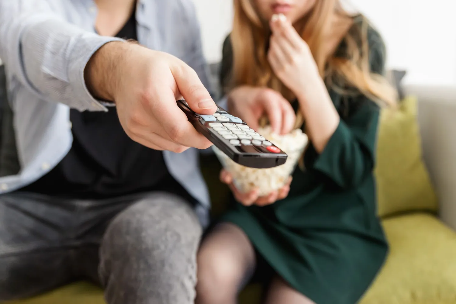 Kanepede oturan iki kişi; biri televizyon kumandasını ekrana doğrultuyor, diğeri kaseden patlamış mısır yiyor