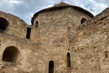 Bulutlu gökyüzü altında yuvarlak kuleli, kemerli pencereleri olan eski taş kale